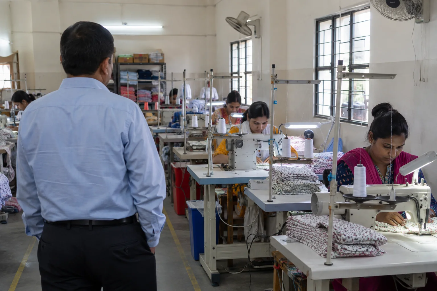 visitor observing cotton garment sewing stations in a modest Indian factory