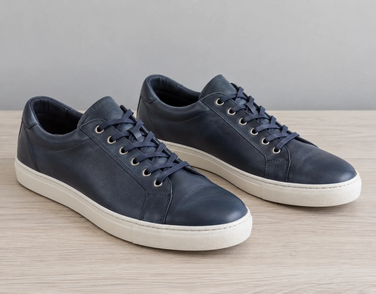Matching navy leather lace-up casual shoes with ivory soles on pale wood