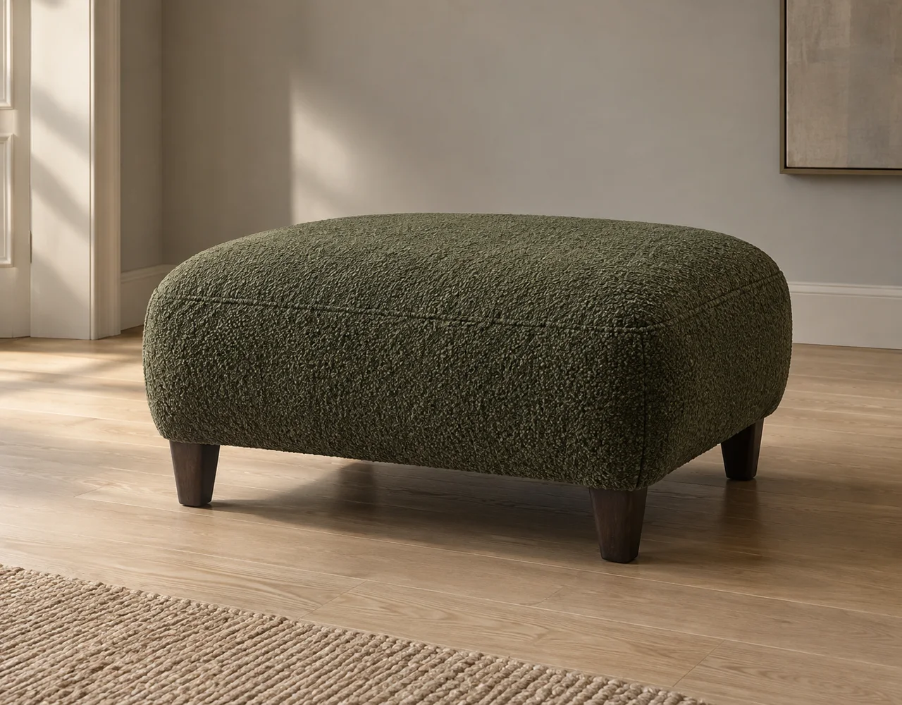 Deep olive textured upholstered ottoman with short dark wooden legs on an oak floor