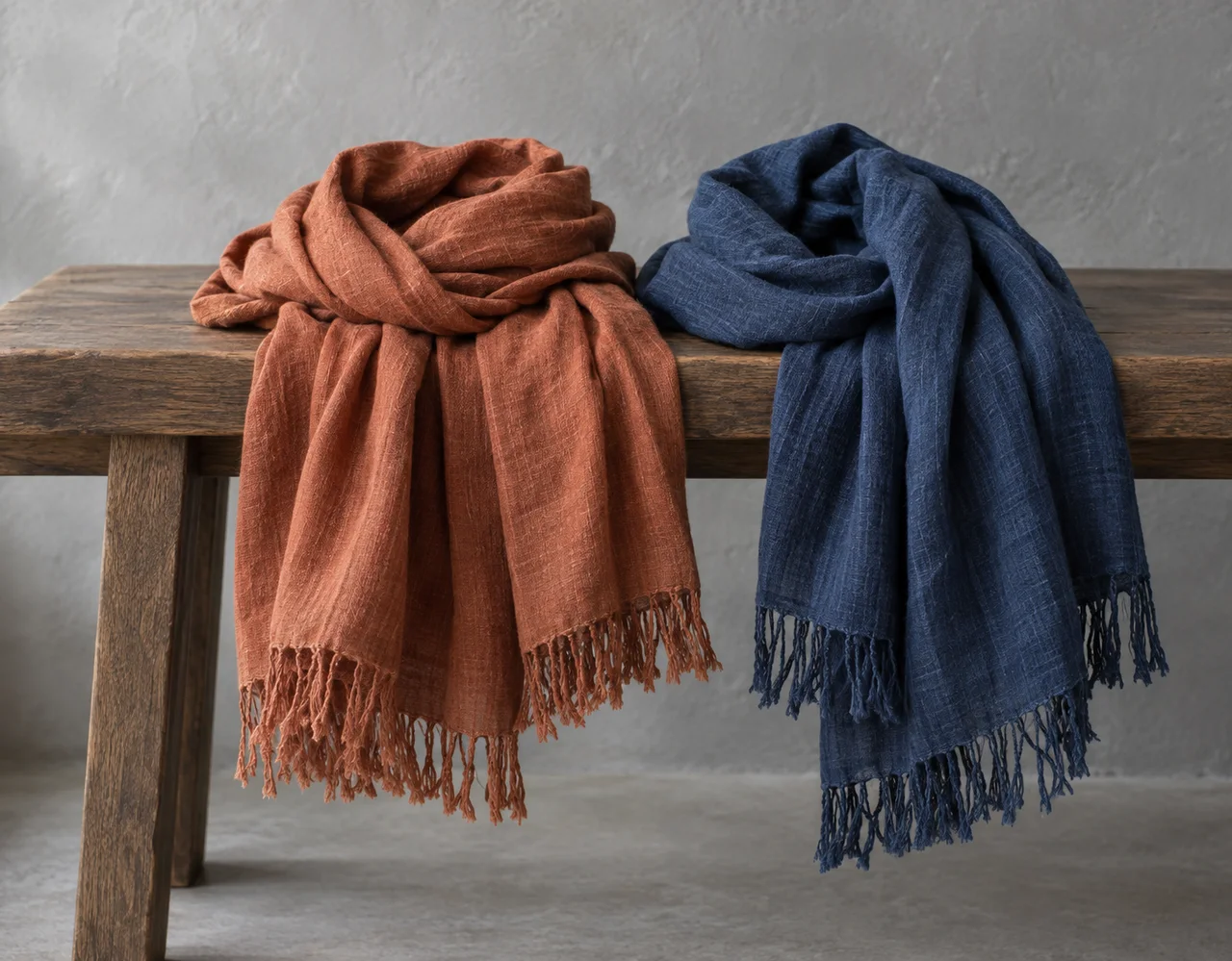Rust and indigo woven scarves with fringed ends draped over a wooden bench